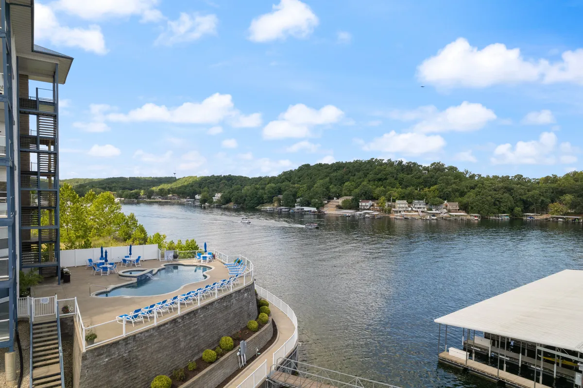 This image captures a bright swimming pool area with views of the lake in the background, surrounded by lush greenery and residential buildings. The poolside area includes comfortable lounge chairs, creating a lively yet relaxing spot for cooling off after outdoor activities.
