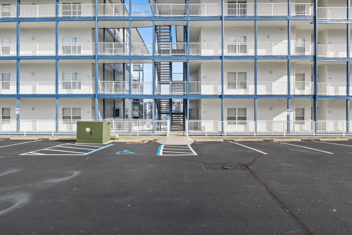 This exterior view highlights the balconies of the residential buildings, a staircase leading to the upper levels, and a parking lot below. The balconies suggest opportunities for outdoor socializing and taking in sunset views, while the communal areas emphasize connection and accessibility.