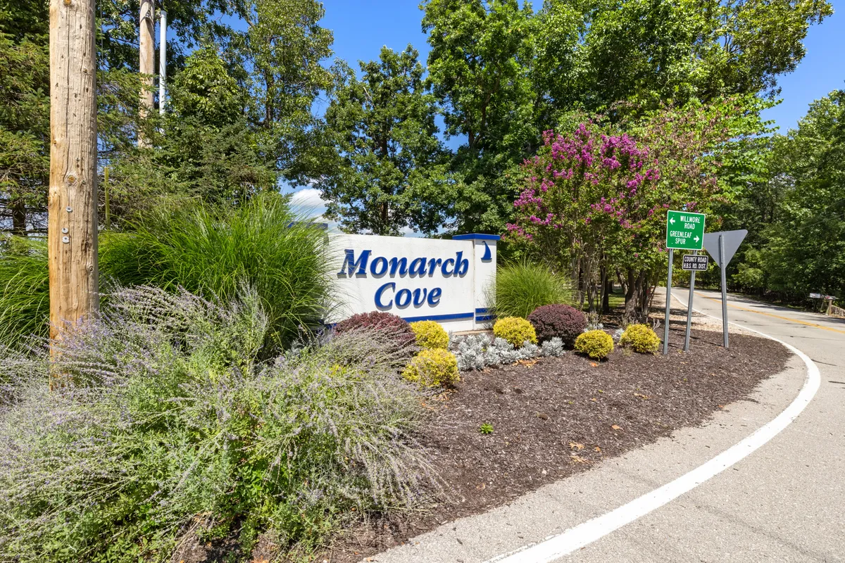 The image features the welcoming Monarch Cove sign at the entrance, surrounded by manicured landscaping and visible traffic signs. The area is serene and hints at families exploring or gathering for local events, setting the scene for community exploration.