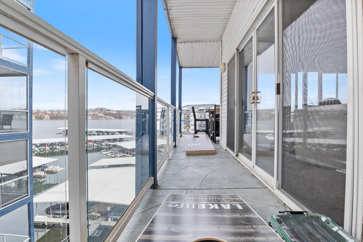 An outdoor seating area with a glass railing, offering expansive lake views. The space includes a fun cornhole game setup, emphasizing both leisure and community activities against the backdrop of the water.