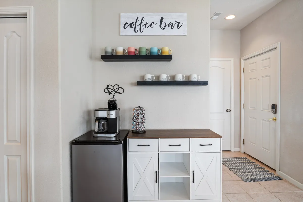 A warm and welcoming coffee bar setup with a prominent coffee maker, shelves lined with colorful mugs, and a decorative 'coffee bar' sign. The cozy, accessible arrangement invites guests to start their day with a fresh brew and easy conversation.