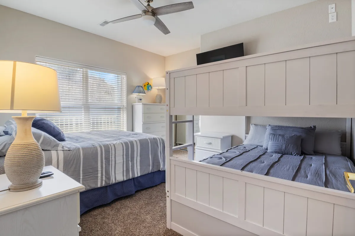 A family-friendly bedroom featuring a bunk bed and a queen-sized bed, complete with a cozy lamp, a dresser, and decorative touches. The space feels relaxed and suitable for both families and friend groups.